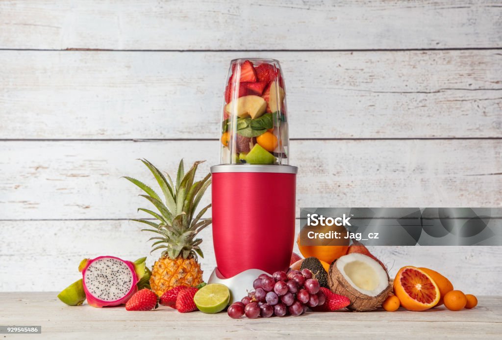Smoothie maker mixer with pieces of fruit ingredients Smoothie maker mixer with pieces of fruit ingredients, placed in wooden interior. Healthy drink and lifestyle Blender Stock Photo