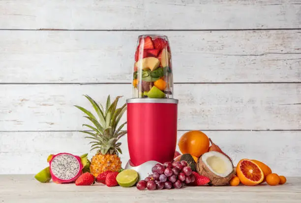 Smoothie maker mixer with pieces of fruit ingredients, placed in wooden interior. Healthy drink and lifestyle