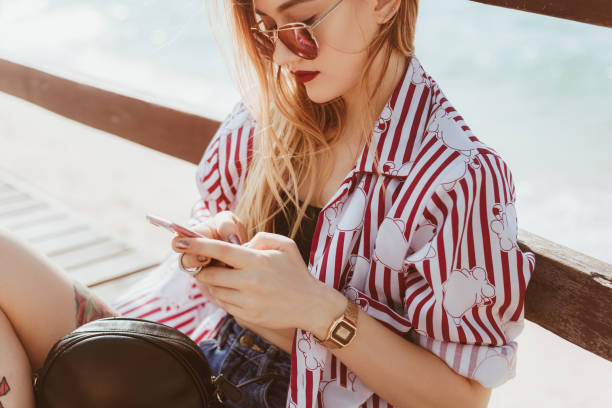 istock stylish young woman using smartphone outdoors while sitting on floor of pier in front of blurred sea 929552186