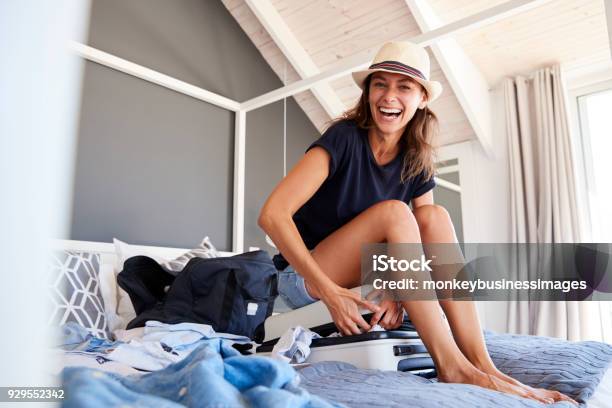 Portrait Of Woman Trying To Close Full Holiday Suitcase Stock Photo - Download Image Now