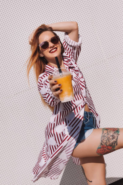 istock beautiful young woman with plastic cup of cocktail leaning back on white wall 929552462