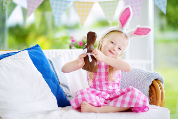 istock Cute little girl wearing bunny ears eating chocolate Easter rabbit 929560058