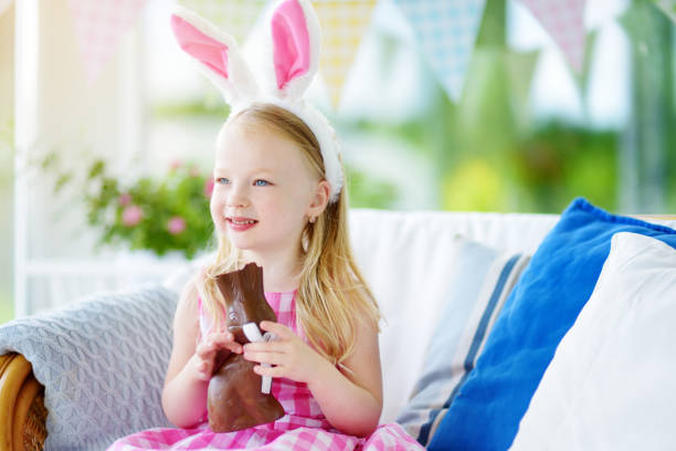 istock Cute little girl wearing bunny ears eating chocolate Easter rabbit 929560160