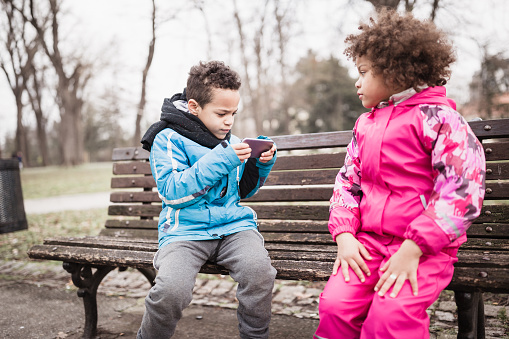 Cute, mixed race brother and sister, playing with mothers mobile phone outdoors in the park