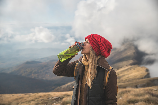 Young woman drinking water after climbing to the mountain peak
