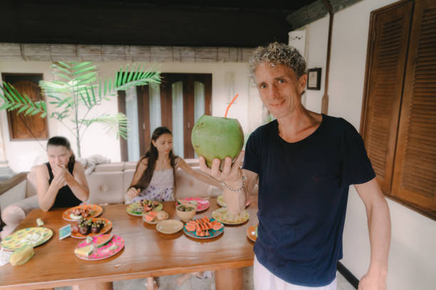 Father passes  young coconut  to family that eats tropical fruits on patio