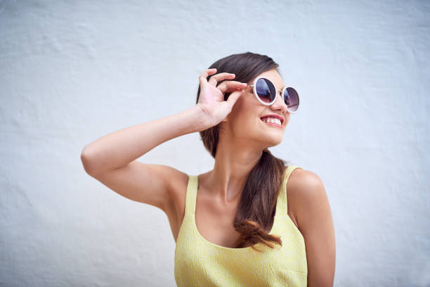 Studio shot of a cheerful young woman wearing sunglasses while posing against a grey background