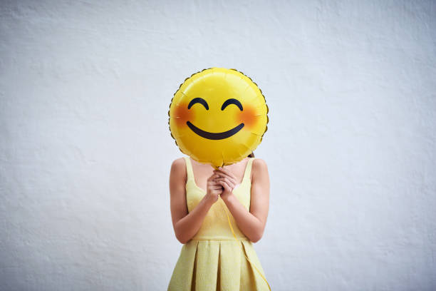 Hold on to your smile and spread the happiness Studio shot of a young woman holding a balloon with a smiley in front of her face rosy cheeks stock pictures, royalty-free photos & images