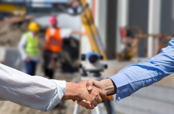 Business people shaking hands at construction site Two business people shaking hands in front of leveling instrument on construction site with workers in background theodolite photos stock pictures, royalty-free photos & images