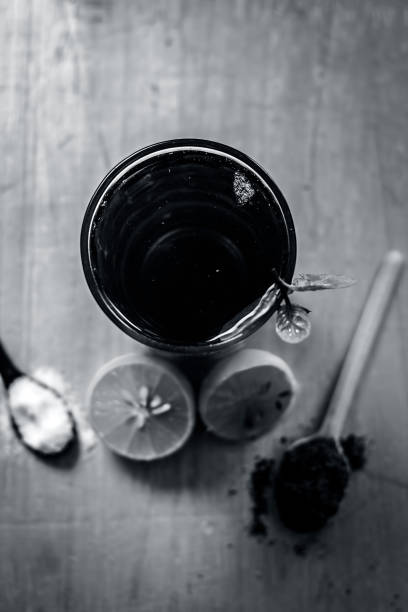 Popular Indian/Asian summer drink Kala Khatta Sharbat with garnishing ingredients i.e. sliced lemon,Citrus Ã limon, salt,sodium chloride, Black pepper and Piper nigrum on silver wooden surface.