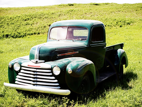 Old green truck sitting in a field on its own. Image has been colorized and lens flare has been added.