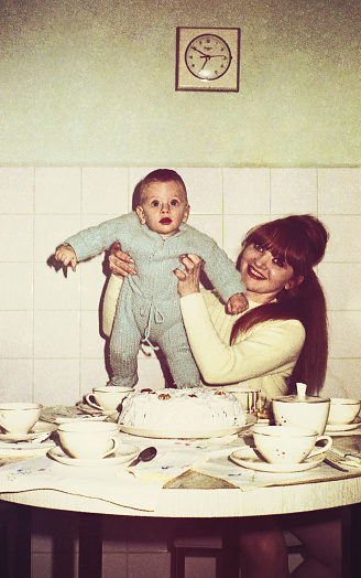 vintage colored image of a mother holding her baby boy in the kitchen.