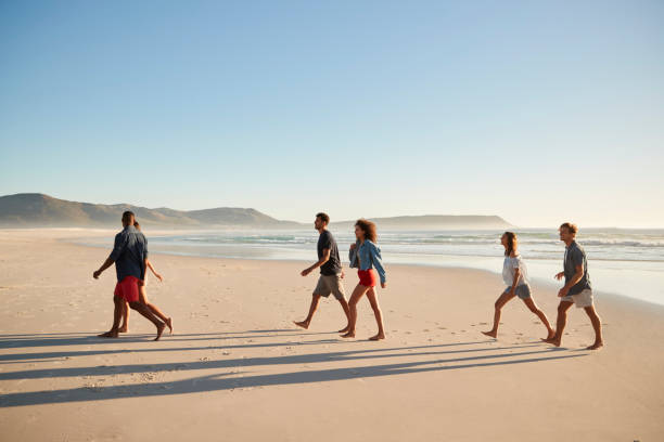 istock Group Of Friends On Vacation Walking Along Beach Together 929701872