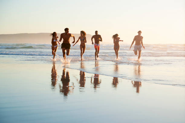 istock Group Of Friends Run Through Waves Together On Beach Vacation 929702122