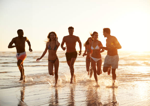 istock Group Of Friends Run Through Waves Together On Beach Vacation 929704848