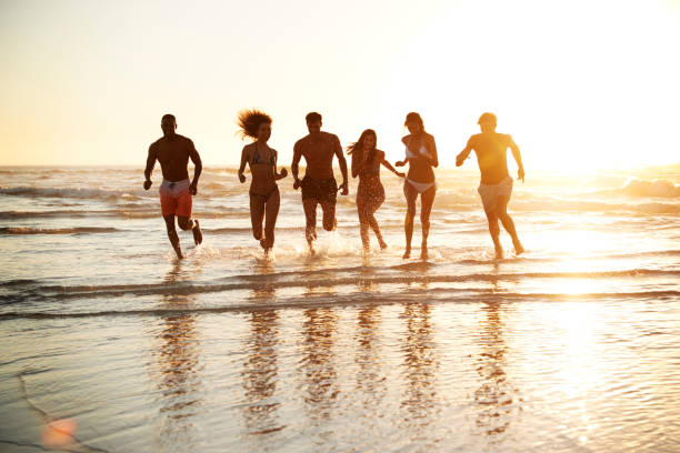 istock Group Of Friends Run Through Waves Together On Beach Vacation 929704850