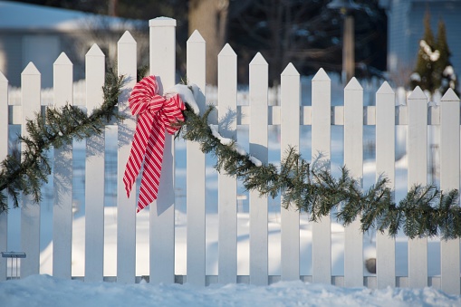 Christmas bow and garland on white picket fence.