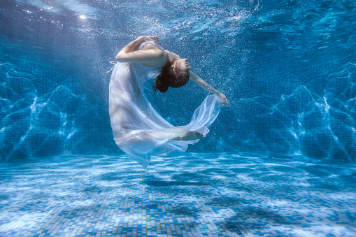 Girl shows the performance under the water, she dances in a white dress.