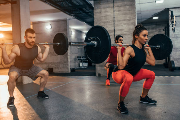 No pain, no gain Shot of two young men and a woman lifting weights at the gym squatting position photos stock pictures, royalty-free photos & images