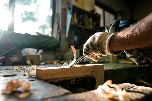An experienced carpenter shapes wood with a chisel.