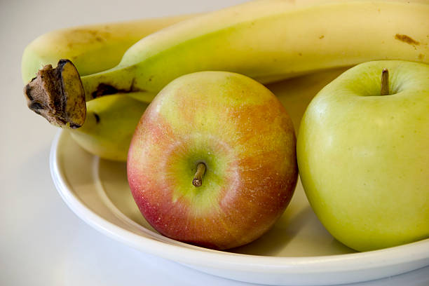 jabłek i bananów na białym talerzu 2 - three objects three people three animals apple zdjęcia i obrazy z banku zdjęć