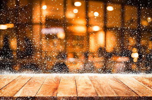 Empty wood table top with snowfall and bokeh cafe restaurant in night winter background.For holiday,christmas day and new year concept.