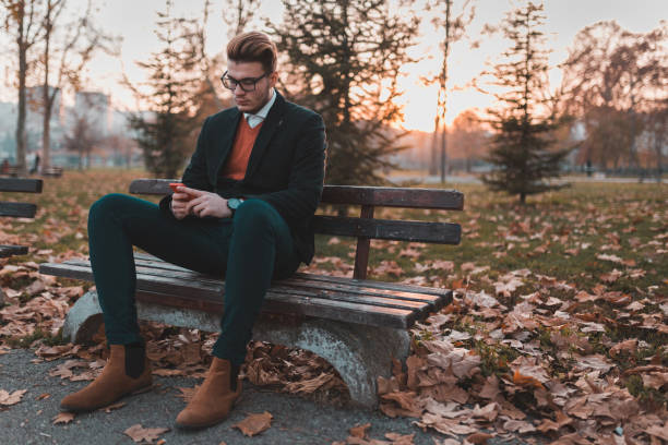 istock Handsome young man sitting on the bench and using phone in the park 929764936
