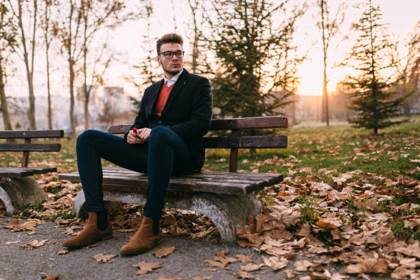 istock Handsome young man sitting on the bench and using phone in the park 929765342