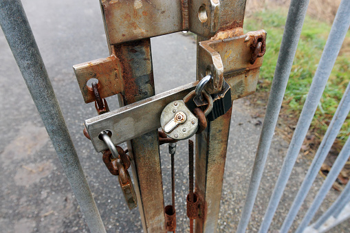 Close-up of half rusted steel gate with three padlocks