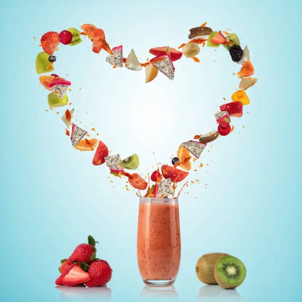 Smoothie drink with fruit flying ingredients in heart shape, isolated on gradient background. Healthy drink and lifestyle