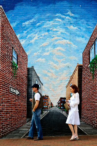 Asheville, North Carolina, USA - April 28, 2012: A man and woman, one carrying a toothpick and the other a cigarette, walk on a city sidewalk past a mural painted on a wall. Asheville is known for its art scene and alternative lifestyles.