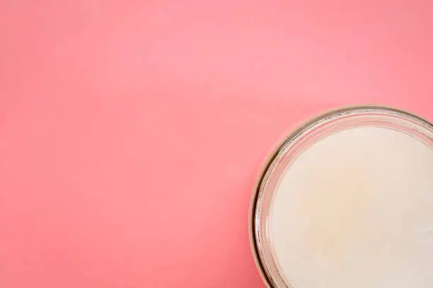 glass jar of coconut cooking oil on a pink background, top view