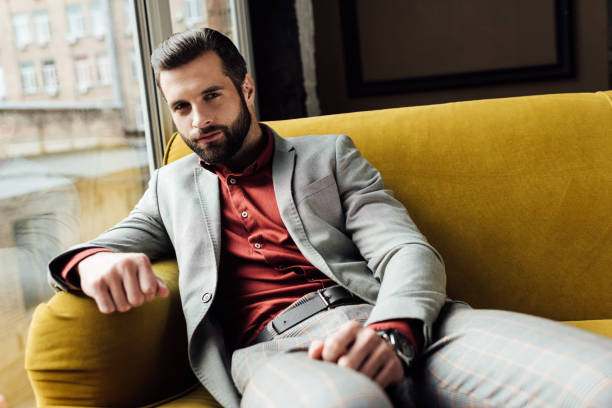 istock stylish bearded man sitting on yellow sofa at window 929803726