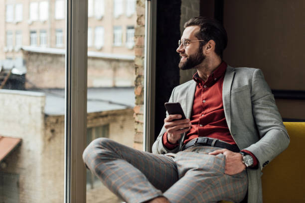 istock handsome smiling man in glasses using smartphone and looking at window 929806262