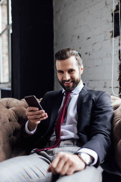 istock handsome smiling businessman using smartphone and sitting in armchair 929818540