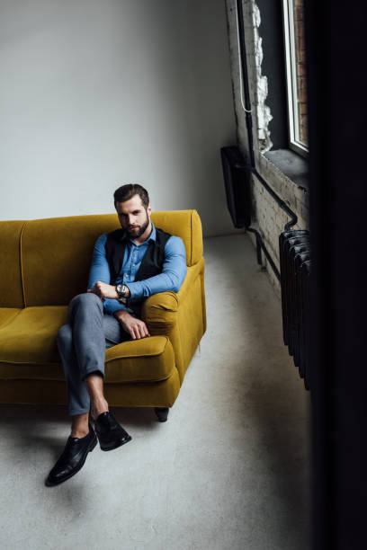istock fashionable elegant man sitting on yellow sofa in loft 929818700