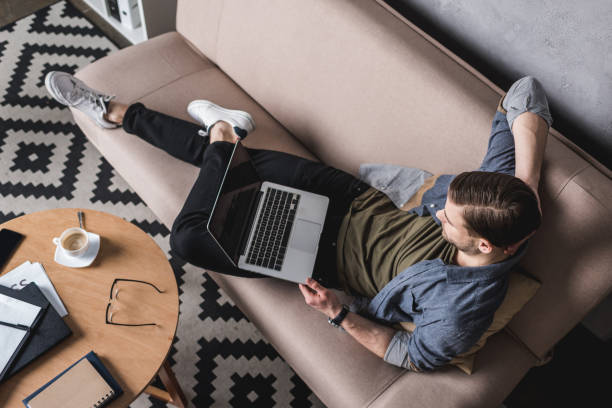 istock high angle view of young man working with laptop on couch 929848958
