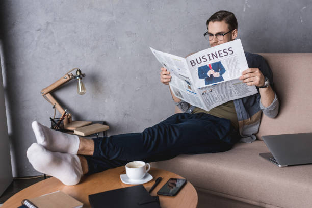 istock young barefoot businessman reading newspaper on couch 929851518
