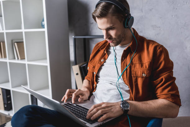 istock young handsome man in headphones working with laptop on couch 929858048