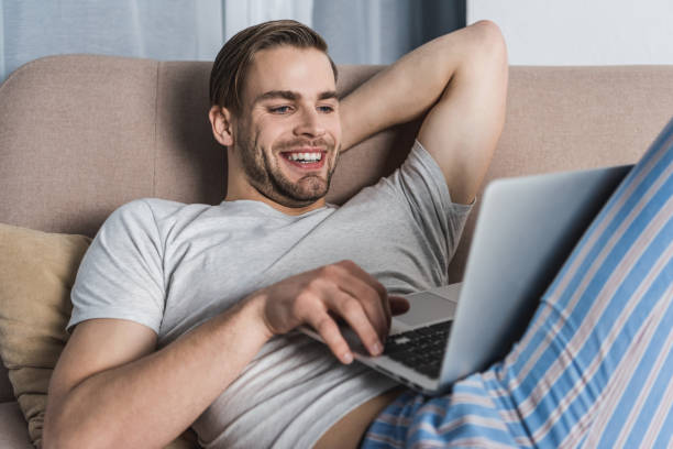istock young smiling freelancer in pajamas working with laptop on couch 929858070