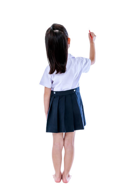 Full body. Back view of young preschool child in uniform. Asian girl writing something with red crayon. Education and people concept. Isolated on white background. Great for your design or text.