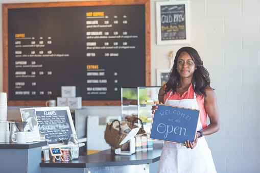 Young female African American coffeehouse owner holds up a sign 
