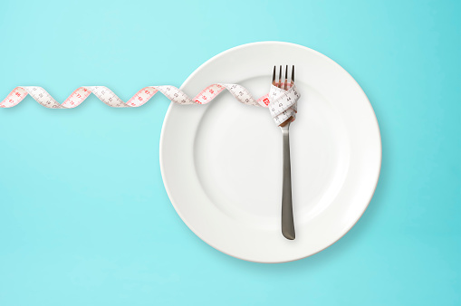 Place setting with steel fork and measuring tape on blue background with copy space.