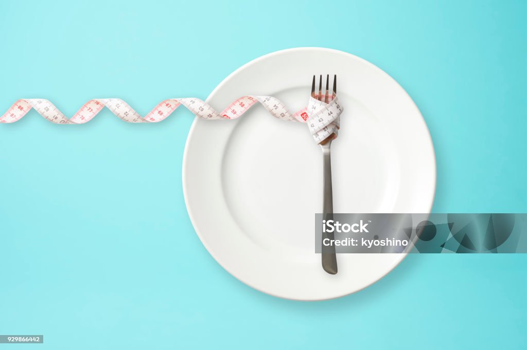 Place setting with steel fork and measuring tape on blue background Place setting with steel fork and measuring tape on blue background with copy space. Dieting Stock Photo