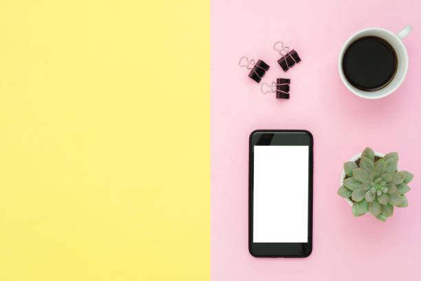 istock Office desk working space - Flat lay top view of a working space with coffee cup, cactus tree and blank mock up phone on pastel background. Pastel pink yellow color background space concept. 929870290