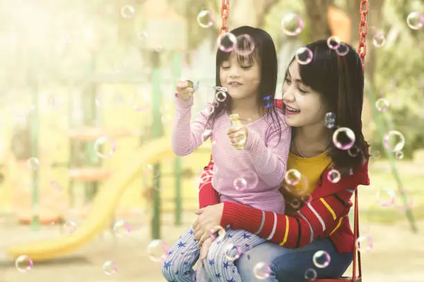 Mother and daughter having fun with soap bubbles at playground. Summer or Spring concept