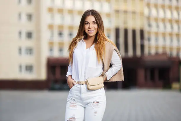Photo of Young fashion woman in white shirt and ripped jeans walking in city street