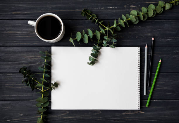 istock Sketchbook and pencils on black wooden table, decorated with green eucalyptus branches. Flat lay, top view 929877818
