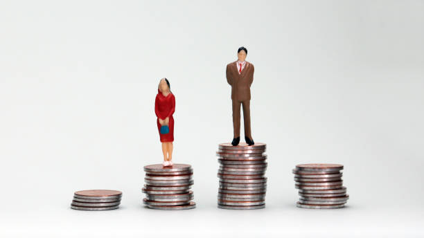 Gender wage difference concept. A miniature man and a woman standing on top of a pile of coins. stock photo