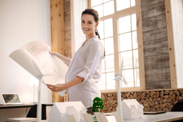 istock Joyful pregnant designer comparing blueprint with model 929908148